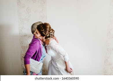 Mom Congratulates The Bride With A Marriage And Hugs. Woman Welcomes. Happy Bride With Mother On Background White Wall In Home. Wedding Ceremony. Close Up.