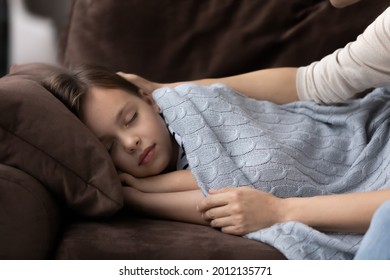 Mom covering sleepy child with blanket or plaid. Loving mother touching, caressing, comforting sleeping daughter girl. Cute peaceful kid taking nap on couch in living room. Child care concept