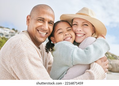 Mom, Dad And Child Hug At The Beach On Family Vacation, Holiday And Enjoying Weekend. Love, Affection And Multicultural Parents With Happy Girl In Portrait Smile, Bond And Embrace By Ocean Together