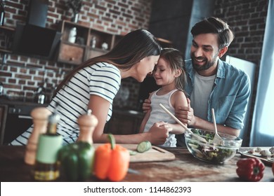 Mom, Dad And Daughter Are Cooking On Kitchen. Happy Family Concept. Handsome Man, Attractive Young Woman And Their Cute Little Daughter Are Making Salad Together. Healthy Lifestyle.