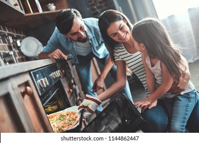 Mom, Dad And Daughter Are Cooking On Kitchen. Happy Family Concept. Handsome Man, Attractive Young Woman And Their Cute Little Daughter Are Making Pizza Together.