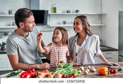 Mom, dad and daughter are cooking on kitchen. Happy family concept. Handsome man, attractive young woman and their cute little daughter are making salad together. Healthy lifestyle. - Powered by Shutterstock