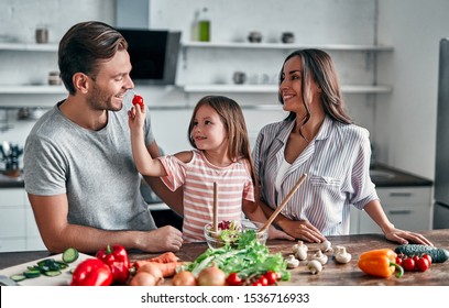 Mom, Dad And Daughter Are Cooking On Kitchen. Happy Family Concept. Handsome Man, Attractive Young Woman And Their Cute Little Daughter Are Making Salad Together. Healthy Lifestyle.