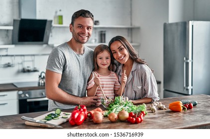 Mom, Dad And Daughter Are Cooking On Kitchen. Happy Family Concept. Handsome Man, Attractive Young Woman And Their Cute Little Daughter Are Making Salad Together. Healthy Lifestyle.