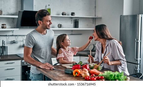 Mom, Dad And Daughter Are Cooking On Kitchen. Happy Family Concept. Handsome Man, Attractive Young Woman And Their Cute Little Daughter Are Making Salad Together. Healthy Lifestyle.