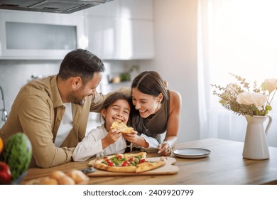 Mom, dad and daughter are eating together at home. Happy family eating pizza at home. - Powered by Shutterstock