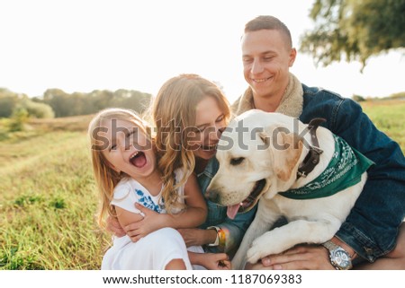 Mom, dad, and daughter having fun playing with big dog in the garden at sunset