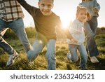 Mom, dad, daughter and son walk in green grass in spring field. Happy young family with children spending time together, running outside, go in nature at sunset. Concept of family holiday outdoors.