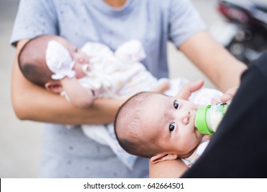 Mom And Dad Help Each Other To Feeding And Holding Their Twin Babies.