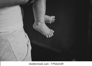 Mom And Dad Are Holding The Baby. The Legs Of The Baby Close-up.