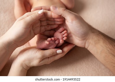 Mom And Dad Are Holding The Legs Of A Newborn Baby