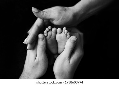 mom and dad holding the legs of a newborn baby black and white photo