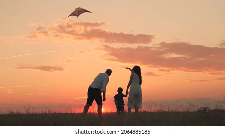 mom dad and kid launch flying kite into sky at sunset, happy family, childhood dream of flying, father, mother and child, travel together on vacation, teamwork, teach baby to play take care and love