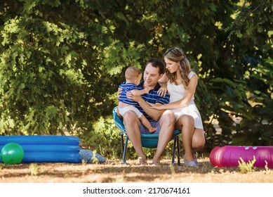 Mom Dad And Little Boy Play In An Inflatable Pool Near A Sun Lounger On The Lawn