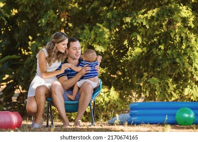 Mom Dad And Little Boy Play In An Inflatable Pool Near A Sun Lounger On The Lawn