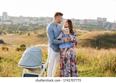 mom, dad and little girl having fun outdoors in the grass on summer day. mother's, father's and baby's day. Happy family for a walk with stoller outside the town. - Shutterstock ID 1741707773