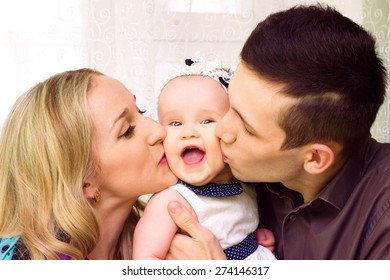A mom and dad parent kissing their young baby