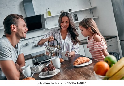 Mom, Dad And Their Little Beautiful Daughter Have Tea Party In The Kitchen And Talk. Happy Family Concept.