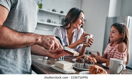 Mom, dad and their little beautiful daughter have tea party in the kitchen and talk. Father puts butter on bread. Happy family concept. - Powered by Shutterstock