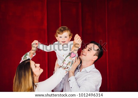 Mom, dad and their little son dressed in casual style pose in a red room