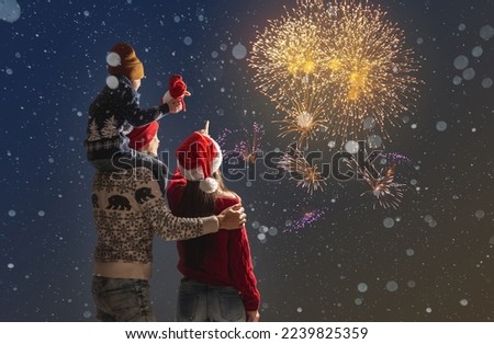 Mom and dad with their son on their shoulders in warm clothes and in a Santa hat. The family celebrates the new year looking at the fireworks outside. Happy Christmas holiday weekend