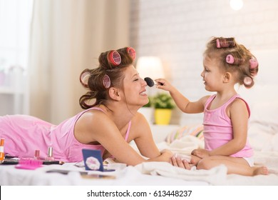 Mom And Daughter In The Bedroom On The Bed In The Curlers Make Up, Paint Their Nails And Have Fun