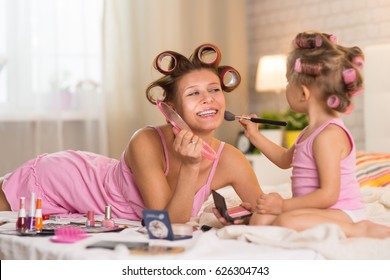 Mom And Daughter In The Bedroom On The Bed In The Curlers Make Up, Paint Their Nails And Have Fun