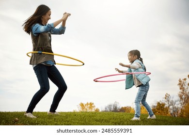 Mom, daughter and dance with hoop in nature, play and field in autumn for activity. Child, together and bonding with female person or mother with girl, outdoor and trees for holiday in park with toys - Powered by Shutterstock