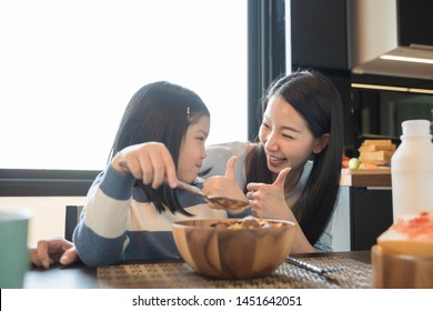 Mom And Daughter Eating Cereals With Milk Having Breakfast In Kitchen.