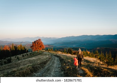 Mom And Daughter, Enjoying Time Together, Walking On Sunset On Top Of Foggy Mountain. Tourists On Background Autumn Nature. Hikers On Sunlight In Trip In Country Europe. Back View. Happy Family.