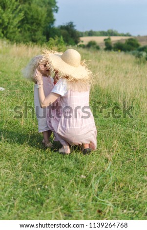 Mom and daughter in the field, dressed in similar dresses and a hat of straw. Happy family relationships, the most warm feelings