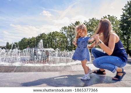 Mom and daughter are fooling around in the park by the fountain.