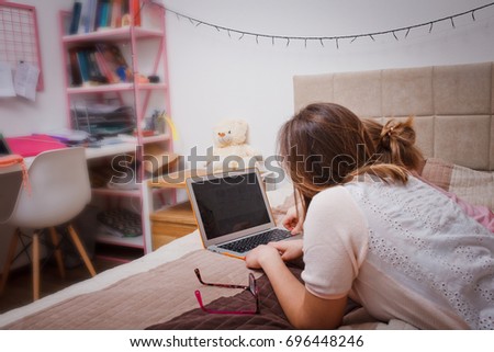 Mom and daughter in glasses lie on the bed in the bedroom and use orange laptop and have fun