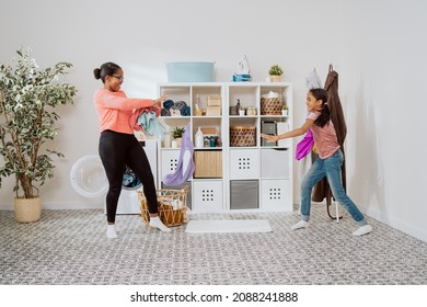 Mom And Daughter Hanging Out In Bathroom Laundry Room Fooling Around Playing Battle For Dirty Clothes Throwing Them At Each Other For Fun Sorting In Background, Dresser With Liquids Washing Machine