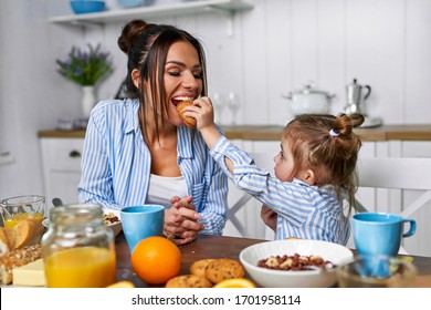 Mom and daughter have breakfast in the morning at home. They eat cereal and croissant with milk. The family spends time together in the kitchen
