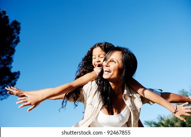 Mom And Daughter Have Fun Outdoors, Smiling And Piggyback In The Sunshine