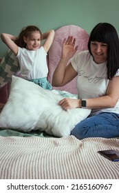 Mom With Daughter Having Fun Pillow Fight On Bed In Bedroom On Weekend Together