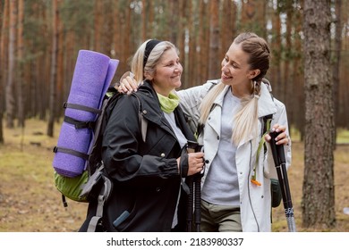 Mom And Daughter Having Fun Together. The Young Woman Hugs The Older Women, Laughing And Talking. Mother Has Backpack, Mat And Trekking Poles Hiking. Doing Sports In The Woods.