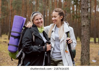 Mom And Daughter Having Fun Together. The Young Woman Hugs The Older Women, Laughing And Talking. Mother Has Backpack, Mat And Trekking Poles Hiking. Doing Sports In The Woods.