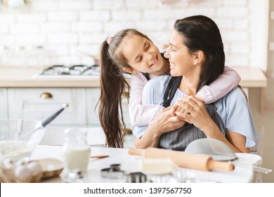 Mom And Daughter In Kitchen. Cute Girl Hugging Mother, Cooking Bakery Together, Empty Space