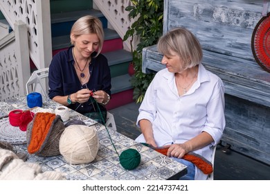 Mom And Daughter Knit Together In The Garden. Family Friendly Leisure. Elderly Mother Teaching To Crochet Adult Daughter 