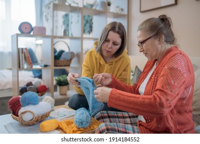 Mom And Daughter Knit Together On The Couch. Family Friendly Leisure. Elderly Mother Teaches To Crochet Adult Daughter In Living Room On Sofa