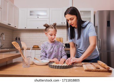 mom and daughter lay out dough in a baking tray. They cook at home in the kitchen. Mother and child daughter girl are cooking cookies and having fun in the kitchen