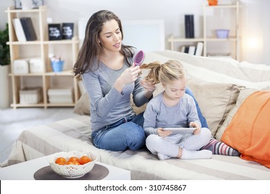 Mom And Daughter In The Living Room. Mother Combing Daughter Hair