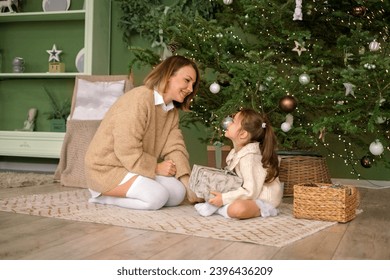 Mom and daughter open Christmas presents early in the morning. Children's happiness to accept gifts in the new year - Shutterstock ID 2396436209