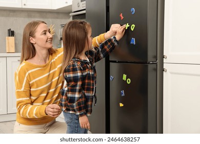 Mom and daughter putting magnetic letters on fridge at home. Learning alphabet - Powered by Shutterstock