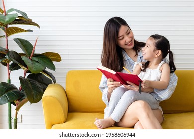 Mom and daughter reading and writing together on couch at home. Happy family and mother's day concept. Asian woman and Caucasian girl in pajamas playing at home. - Powered by Shutterstock