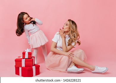 Mom And Daughter In Same Pink Outfit Posing In Great Mood In Pink Studio With Red Gift Boxes