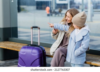 Mom and daughter are sitting at the bus stop and waiting for the bus. Mom shows something to her daughter in the distance - Powered by Shutterstock