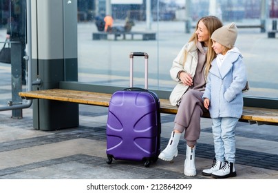 Mom and daughter are sitting at the bus stop and waiting for the bus. Mom shows something to her daughter in the distance - Shutterstock ID 2128642049